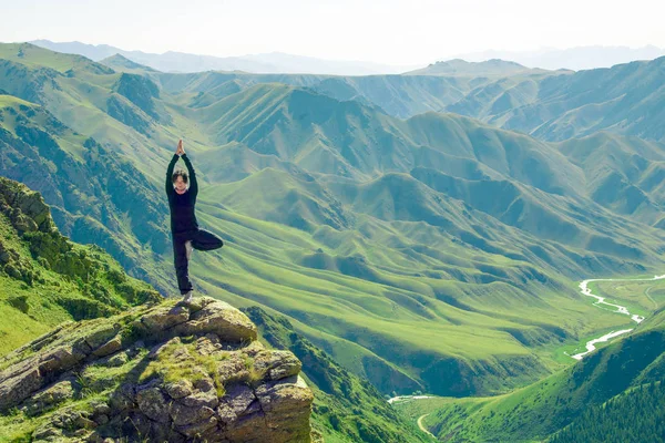 Ein Mädchen in Yoga-Pose steht in den Bergen auf einem der — Stockfoto