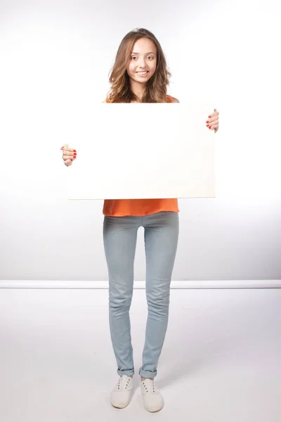 Söt leende flicka som håller ett tomt vitt ark på vit bakgrunds — Stockfoto