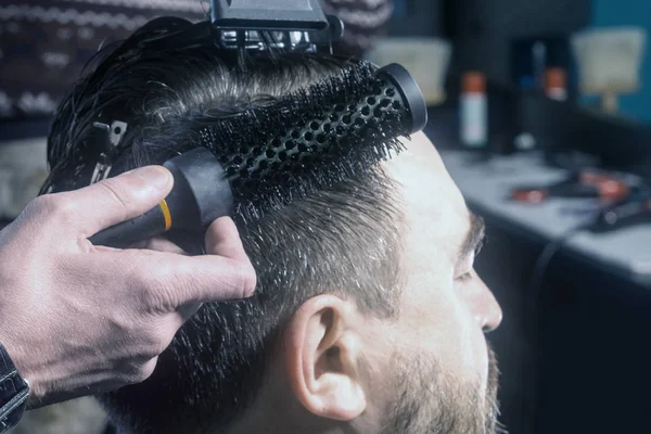 Le coiffeur sèche et coiffe les cheveux coupés par un homme. Gros plan . — Photo
