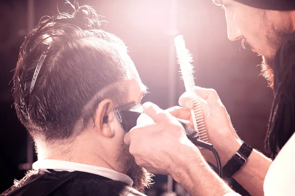 Friseur schneidet einem Mann mit Bart einen modernen Haarschnitt. — Stockfoto