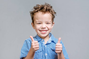 Mavi gömlekli başparmak gri bir arka plan üzerinde gösterilen boy gülümseyerek.