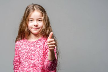 Sevimli kız gri bir arka plan üzerinde kırmızı bir elbise başparmak gösterir.