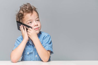 Ciddi bir çocuk üzerinde masada otururken telefonda konuşurken