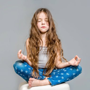 Gri bir backgroun üzerinde lotus pozisyonda meditasyon küçük kız