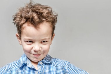 Gri bir arka plan üzerinde mavi gömlek gülümseyen küçük çocuk.
