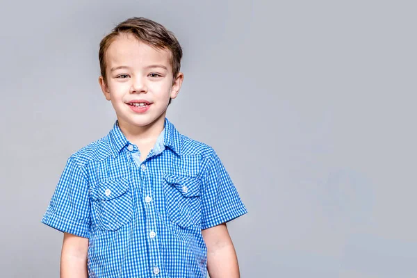 Bonito menino sorridente em azul camisa xadrez no fundo cinza . — Fotografia de Stock