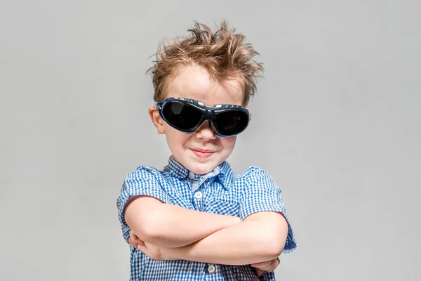 Güneş gözlüğü gülümseyen çocuk gri bir backgro üzerinde göğsünde geçti — Stok fotoğraf