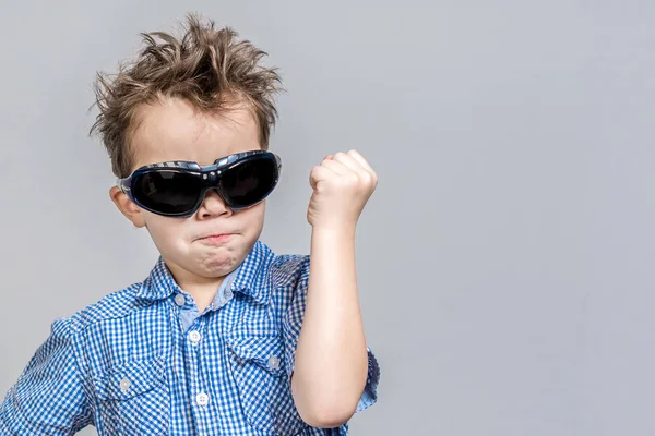Little boy in sunglasses threatens with fist on a gray backgroun — Stock Photo, Image
