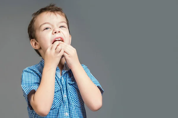 Niño en una camisa azul comiendo mandarina sobre un fondo gris . — Foto de Stock