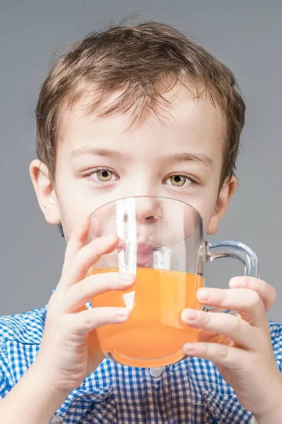 Mavi gömlekli sevimli çocuk gri bir backgroun üzerinde portakal suyu içiyor — Stok fotoğraf