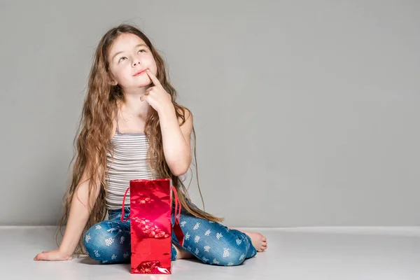 Thoughtful girl sitting near a red gift bag.