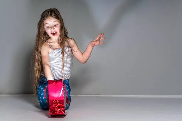 Chica sorprendida recibe un regalo de un paquete rojo en un backgrou gris —  Fotos de Stock