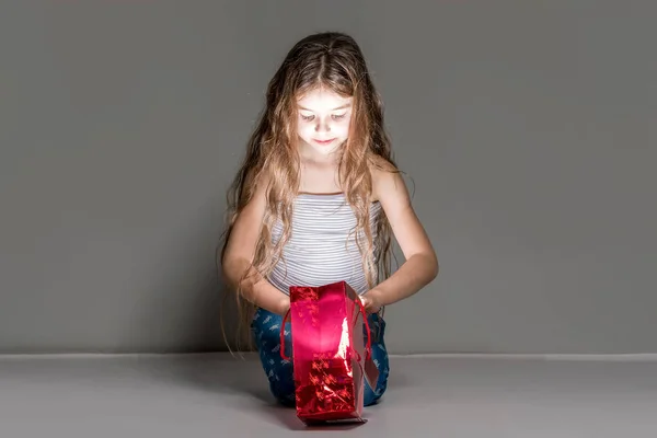 Linda chica abre bolsa de regalo roja sobre fondo gris . —  Fotos de Stock