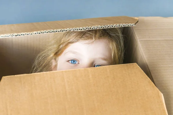 Mała niebieskooka dziewczyna patrząc z kartonowego pudełka, zbliżenie. — Zdjęcie stockowe