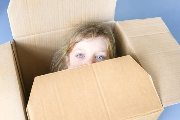 Sad little blue-eyed  girl inside a cardboard box, close-up.