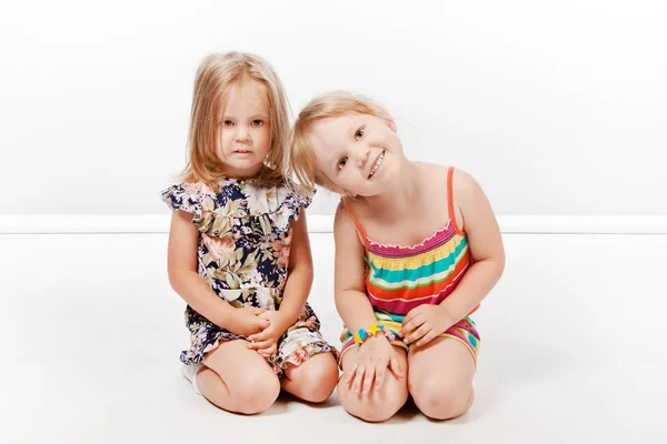 Two little blonde sisters on a white background.