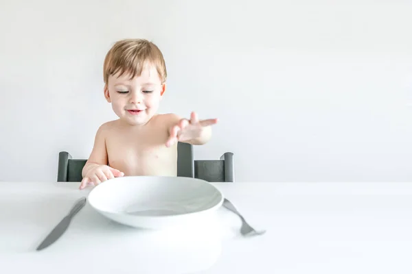 Lindo chico rubio sentado en la mesa con un plato blanco vacío, f —  Fotos de Stock