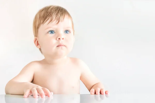 Retrato de un lindo bebé rubio de ojos azules sentado en una mesa en un —  Fotos de Stock