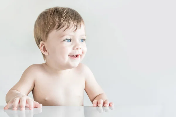 Смеющийся белокурый голубоглазый ребенок сидит за столом . — стоковое фото