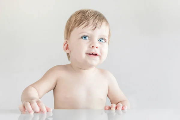 Smiling blond blue-eyed babe sits at the table. — Stock Photo, Image