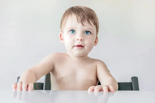 Retrato de un lindo bebé rubio de ojos azules sentado en la mesa clo —  Fotos de Stock