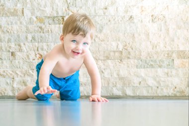 Gülen mavi gözlü sarışın bebek yerde sürünerek.