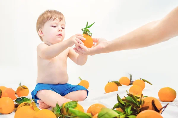 Lindo bebé rubio toma naranja de las manos de su madre . — Foto de Stock