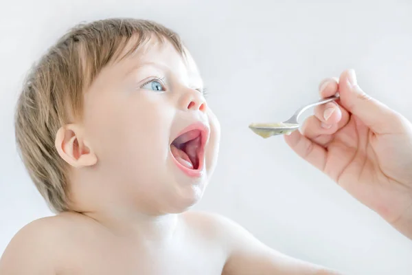 Anne yardımı ile bebek maması yiyen sevimli küçük mavi gözlü çocuk. — Stok fotoğraf
