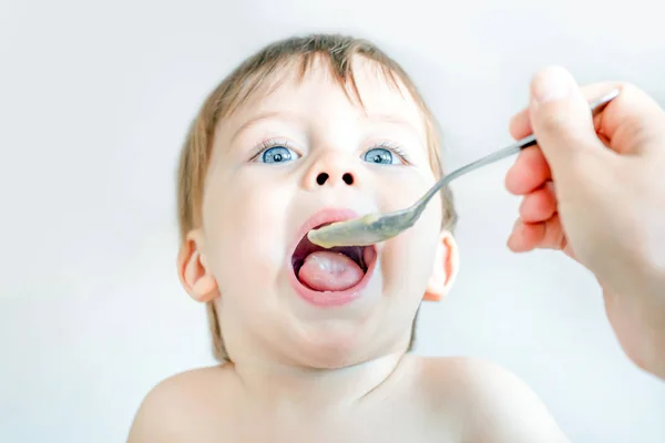 Cuchara alimentando a un pequeño bebé rubio de ojos azules . — Foto de Stock