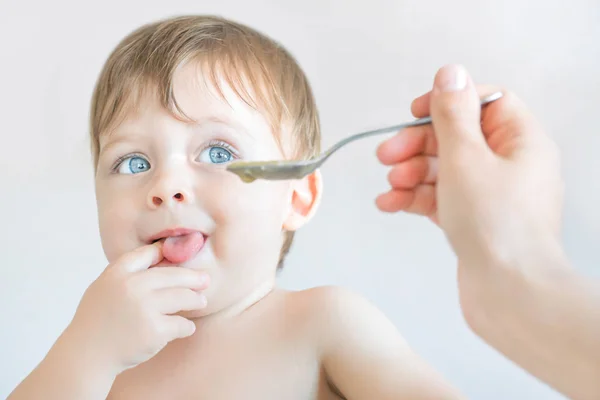 Alimentar a un bebé rubio de ojos azules con una cuchara . — Foto de Stock