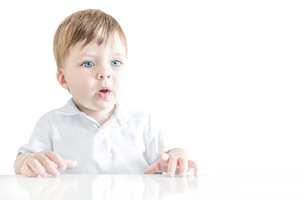 Retrato de um bebê loiro com olhos azuis sentado à mesa . — Fotografia de Stock