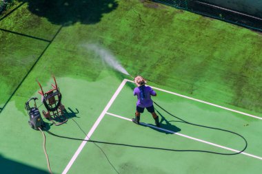 Erkek işçi tenis kortunu su basıncıyla yıkıyor..