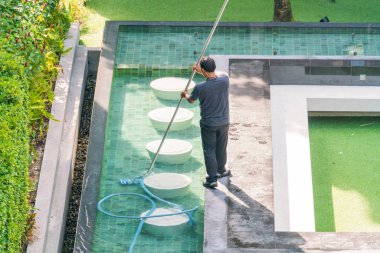 Erkek işçi yüzme havuzunu fırça ve süpürgeyle temizliyor..