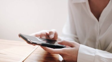 Genç Asyalı kadın ofiste akıllı telefonla çalışıyor.