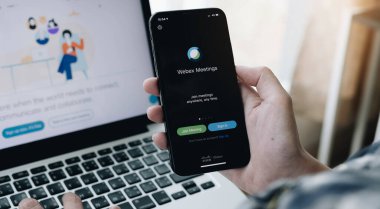 Chiang Mai, Tayland - 14 Nisan 2020. Webex uygulamalı iPhone tutan kadın buluşması. Video konferansı, sosyal uzaklık ve ev işi uygulaması