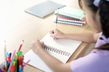 Genç bir kız, parlak bir çalışma ortamında öğrenmeye olan bağlılığını göstermek için defterine özenle yazıyor..