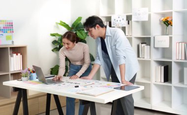 Dijital bir proje üzerinde çalışan iki UXUI tasarımcısı, parlak ve modern bir çalışma alanında tasarım ve stratejileri analiz ediyorlar..