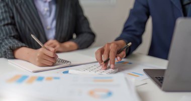 Bütçe tahminleri ve veri içgörülerini tartışmak için bir hesap makinesi ve not defteri kullanan iki iş adamı mali analizde yer aldı..