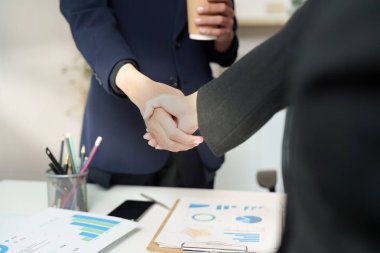 İki iş adamı el sıkışıyor, mali stratejiler ve performans ölçümleri hakkında görüştükten sonra anlaşma imzalıyor.