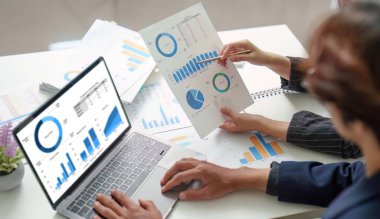 Mali verilerin ortak analizine katılan iki profesyonel, tartışmalarını geliştirmek için raporlar ve bir dizüstü bilgisayar kullanıyorlar..