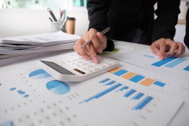 Bir iş adamı, veri analizinde doğruluğu güvence altına alarak tablolar ve raporları incelerken finansal rakamları da hesaplar..