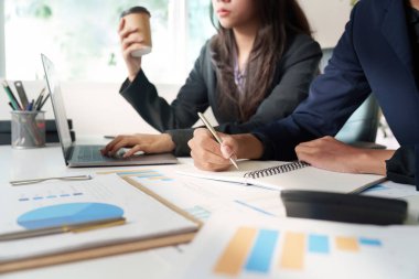 İş kadını elinde kahve fincanı tutarken finansal stratejilere odaklanmış profesyonel bir toplantıda dizüstü bilgisayara not alıyor..