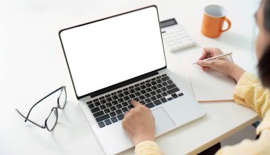 Uzaktan çalışmada organizasyonun önemini vurgulayan, dizüstü bilgisayarda çalışırken notlar yazan bir birey.