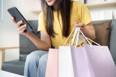 Genç bir kadın elinde renkli alışveriş torbalarıyla telefonuna bakarken gülümsüyor. Perakende terapi ve tüketici sevinci kavramı.