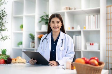 Gülümseyen bir diyetçi, bir karşılama kliniğinde kişisel beslenme planları olan hastalara yardım etmek için hazırlanmış bir pano tutuyor..