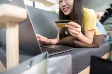 Bir kadın elinde kredi kartı tutarken dizüstü bilgisayarını online alışveriş için kullanıyor. E-ticarette kolaylık kavramı.