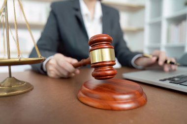 Profesyonel davalı bir avukat dizüstü bilgisayar üzerinde çalışırken bir elinde tokmak tutarak adaleti ve yasal işlemleri sembolize ediyor..