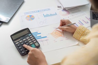 Bir iş analisti etkili yönetim için mali özet raporları ve grafikleri yorumlamak için bir hesap makinesi ve kalem kullanır.