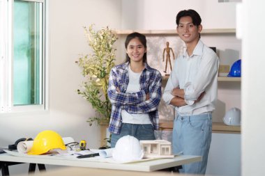 İki mühendis gülümsüyor ve parlak bir ofiste tasarımlar yapmak için işbirliği yapıyorlar. Mühendislikte takım çalışması ve yenilik kavramı.