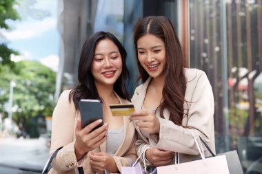 Kara Cuma alışverişinden zevk alan iki kadın, ellerinde akıllı telefon ve kredi kartıyla alışverişlerini ve ödemelerini kontrol ediyorlar..